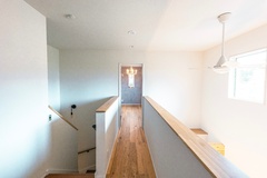 階段からつながる明るい2階ホール。吹き抜けのおかげで光と風がめぐり、心地よい開放感が広がり、木材と白壁の組み合わせが温かみを感じさせるデザインである。