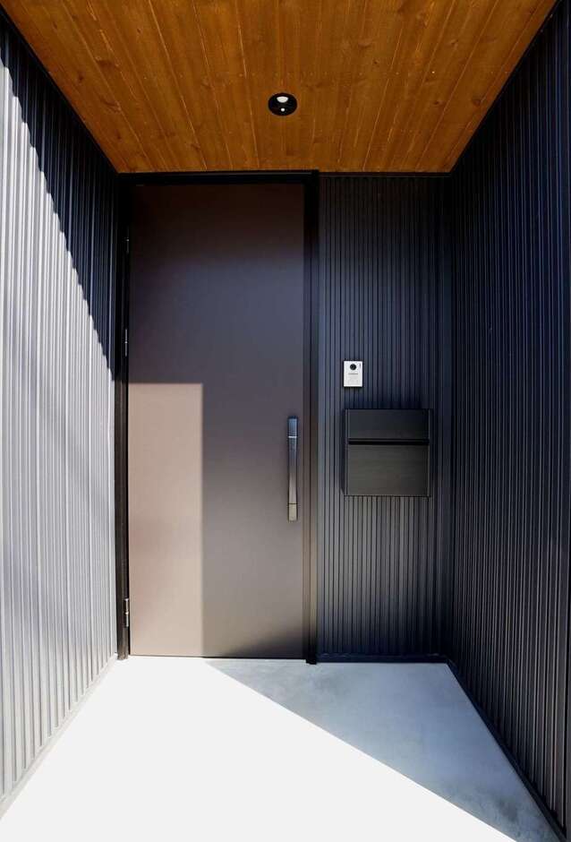 ガルバリウムの外壁とレッドシダーの軒天がバランス良く調和した玄関ポーチ。深い軒に守られて、雨の日もストレスフリー