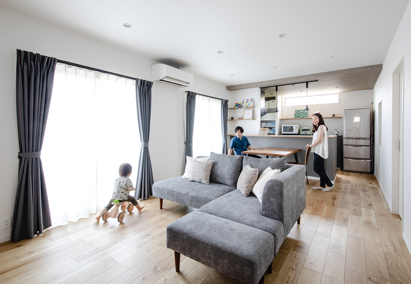 カナメクラフト（かなめ創建）【デザイン住宅、子育て、間取り】18畳のLDKは日当たり抜群。白とグレーでコーディネートされた天井高2,500mmの空間は、キッチンを下がり天井にしたことで、より広く感じられる