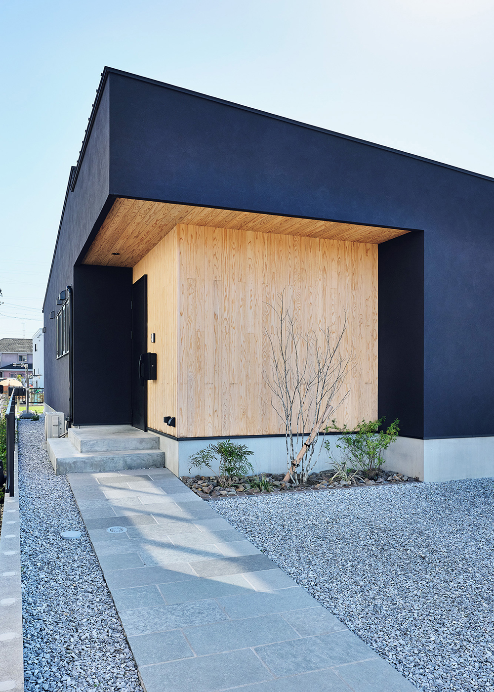 平屋建築ブルーハウス【デザイン住宅、間取り、平屋】石畳風タイルのアプローチ。スギ板張りの玄関ポーチに植栽の緑が映える