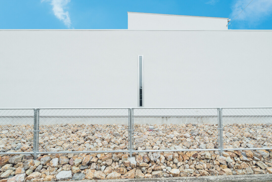 チェックハウス｜フェンスに囲まれたシンプルな外観。白い壁が空と調和し、建物全体が明るく整った印象を与える。