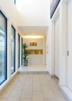 玄関の上部は吹き抜けになっていて開放的。北側をガラス張りにしたことで、日中は照明なしでも柔らかい光が入り込む。そして愛車も眺められる。正面にはガラスタイルを使った縁起ものを飾る棚をデザインした。シューズクロークも設置されているため、いつでもキレイをキープできる