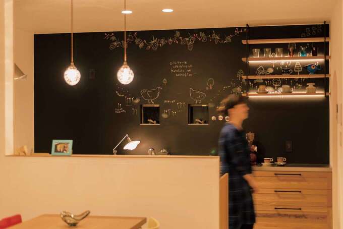黒板&磁石塗料で塗装した壁面には、ふくだのぞみさんのチョークアートが。ウッディなシステムキッチンと、間接照明を仕込んだ吊り下げシェルフがカフェのよう
