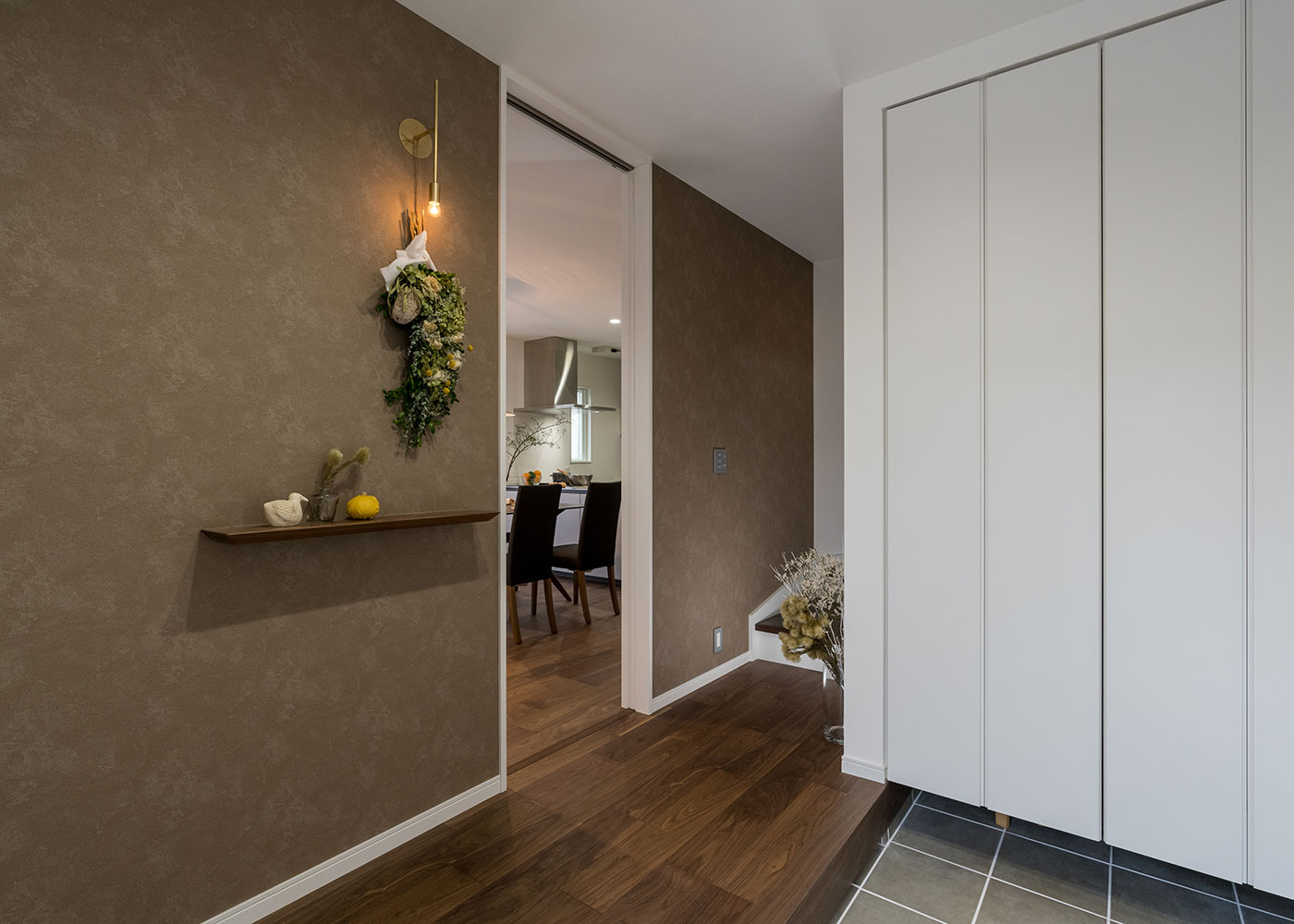 寺田工務店【デザイン住宅、省エネ、間取り】玄関ホールは、柔らかな光でゲストを迎える真鍮のブラケットライトがポイント。季節によって飾り棚のインテリアを変えて楽しむことも。天井まで届くハイドアが空間をより広く見せている