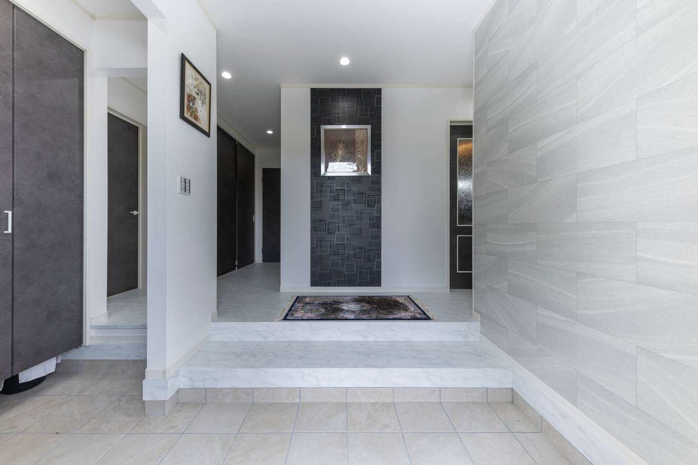 サンワ開発【デザイン住宅、収納力、ガレージ】広々とした玄関から、スタイリッシュな雰囲気。正面の壁には、絵画を飾ることを想定して、アクセントのクロスを採用した。左側のシューズクロークは容量もたっぷり