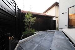 プライベート感のある落ち着いたテラスエリア。黒を基調としたフェンスと石畳の床がシックな印象を与える。植栽がさりげなく配置され、外部からの視線を遮る役割を果たしている。