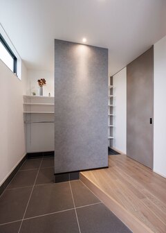 グレーを基調にコーディネートした玄関ホール。斜めに切った框と、天井まで届くハイドアが空間を広く見せている。シューズクローゼットの手前に設けた壁には、目隠しと空間のアクセントという2つの要素を持たせている。壁を境に、日常の動線と来客時の動線がシンプルに分けられている