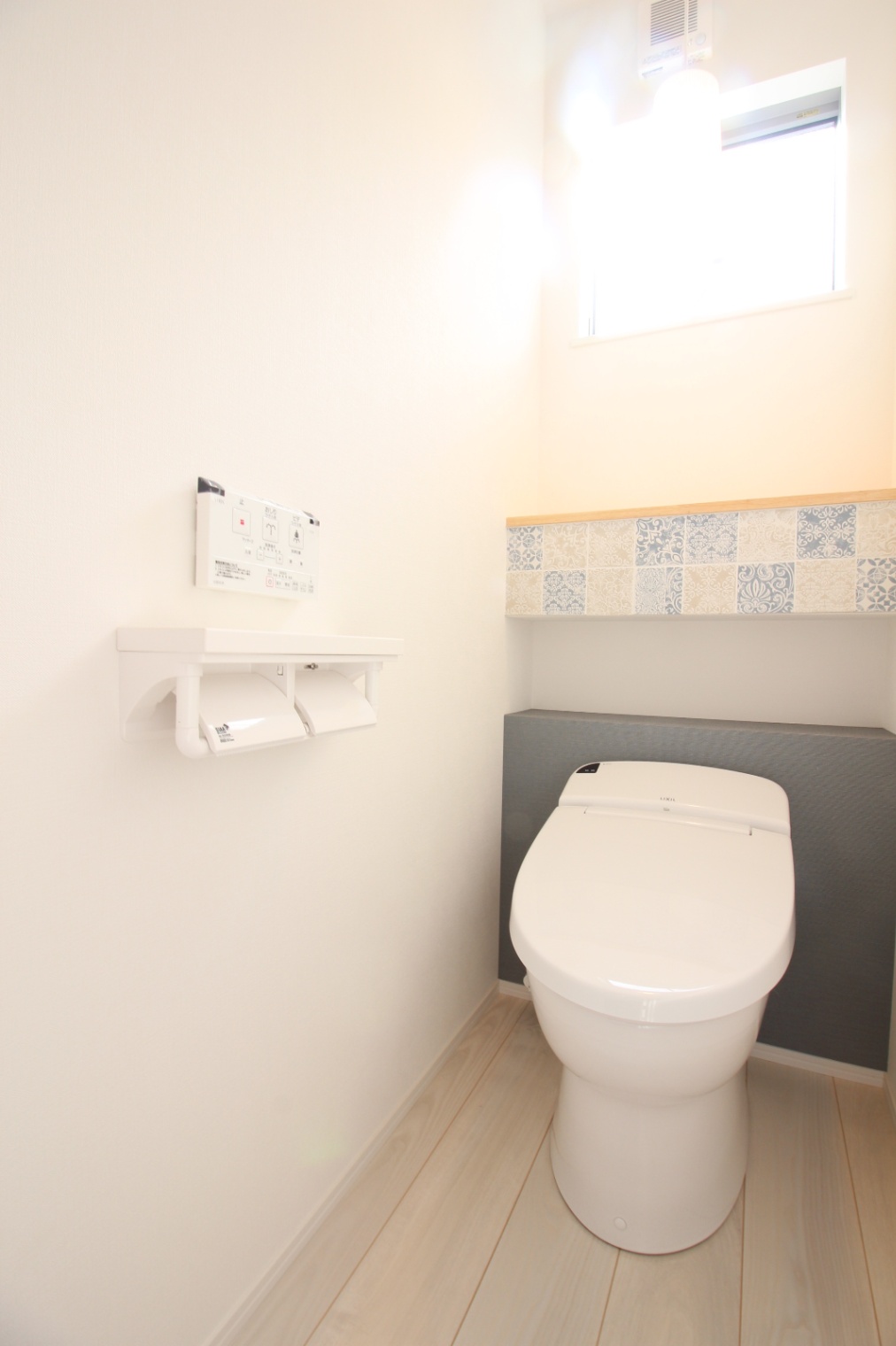 小野田産業～designers house project～｜薄いブルーの甘すぎないタイルがアクセントのトイレ空間。上部の窓から自然光が入り、明るく清潔感のある雰囲気を演出している。