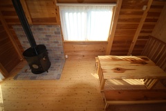 木材を基調にしたダイニングスペース。薪ストーブが設置されており、温かな光が居心地の良い雰囲気を作り出す。素朴な家具が家庭的な温もりを感じさせる。