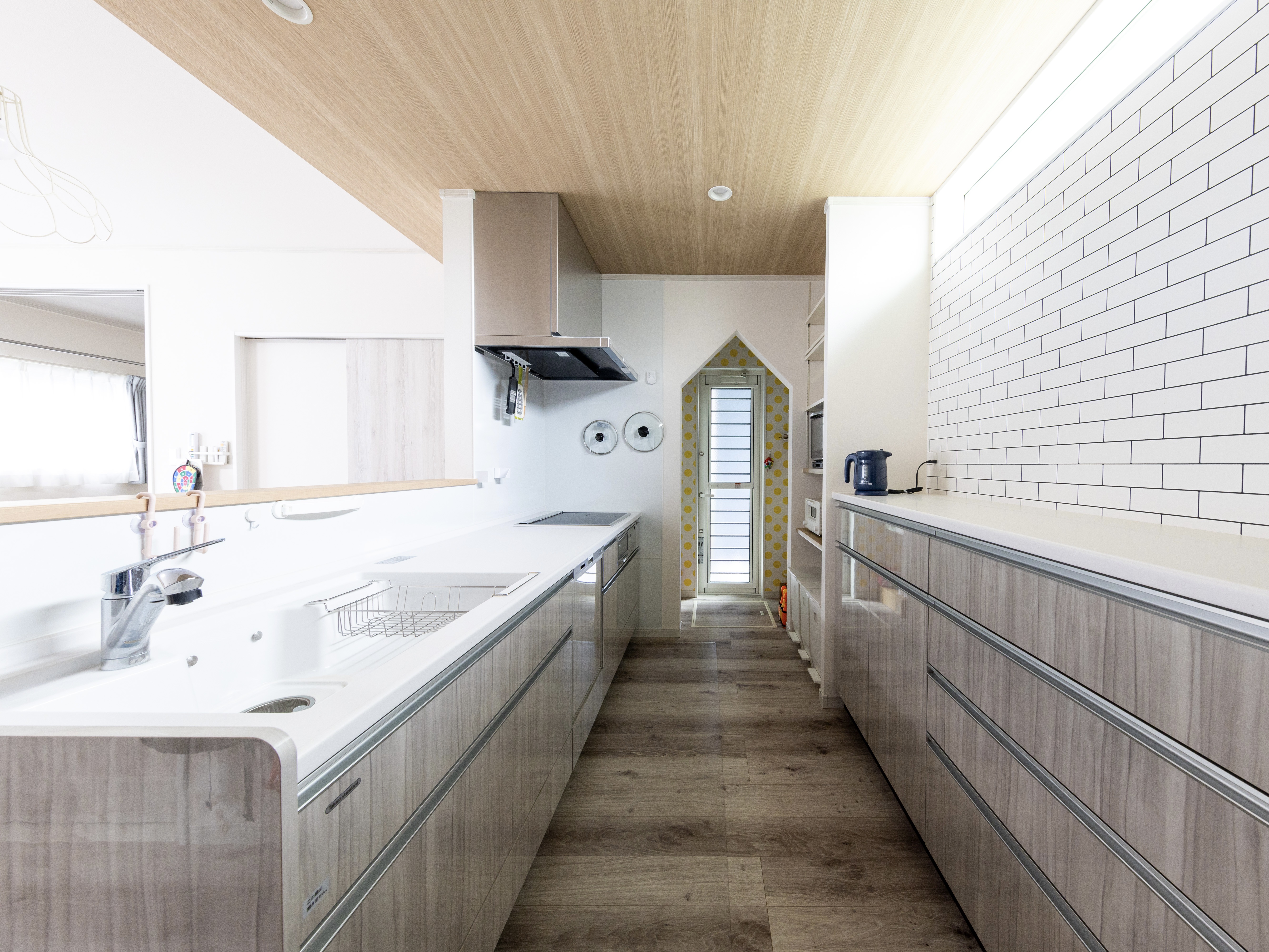 エスホーム｜ウッディで洗練されたデザインのキッチン。収納スペースが豊富で使いやすく、料理がはかどる快適な空間が広がっている。天井の木目調と白タイルの壁がナチュラルモダンな雰囲気を演出している。