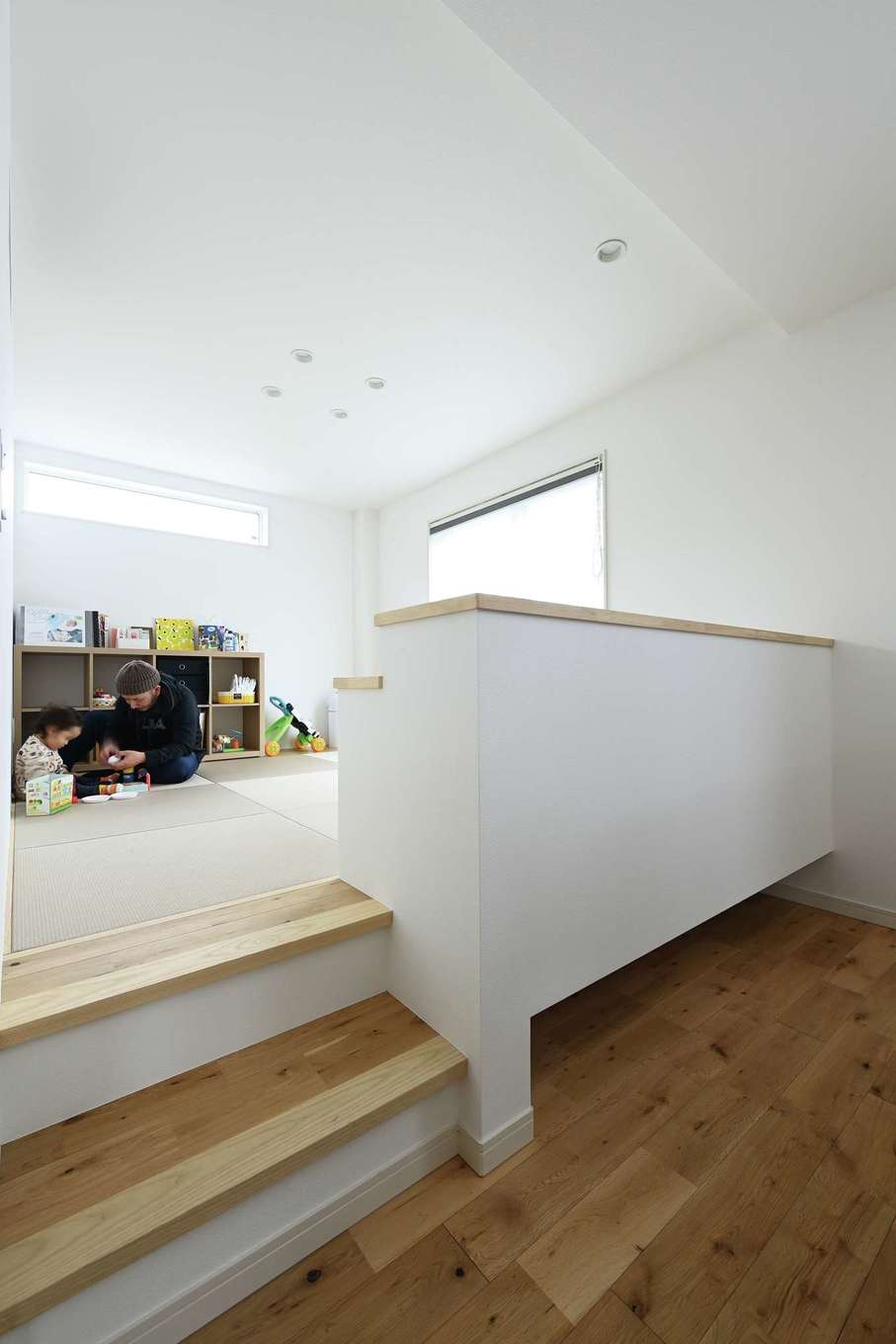 Yamaguchi Design 【デザイン住宅、収納力、間取り】リビングの隣に階段付きの小上がりを設置。仕切壁の下をオープンにしてロボット掃除機が通れるように工夫されている。小上がりはキッズコーナーとして利用可能。おもちゃがリビングまで広がらずに済むので、LDKをスッキリ・キレイに保てる