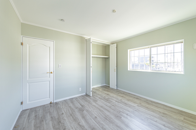 明るい窓から光が差し込む居室スペース。シンプルなデザインで、自由に家具を配置できる広々とした空間。白を基調としたクロスと床材が、清潔感を演出している。