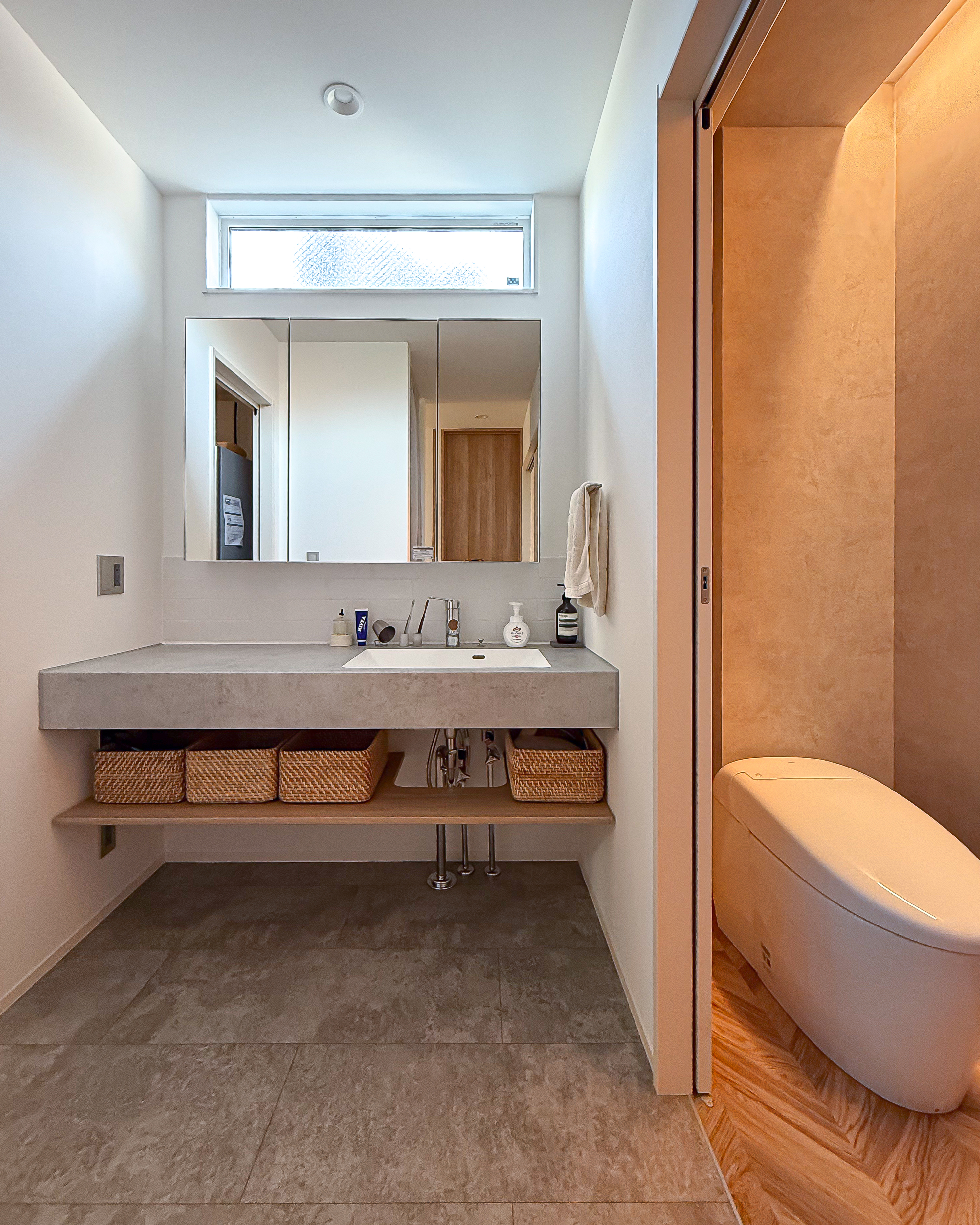 ロイヤルウッド｜広々とした洗面スペースで、収納バスケットを活用した清潔感のあるデザインが特徴。右側にはスタイリッシュなトイレが配置され、機能性も兼ね備えている。