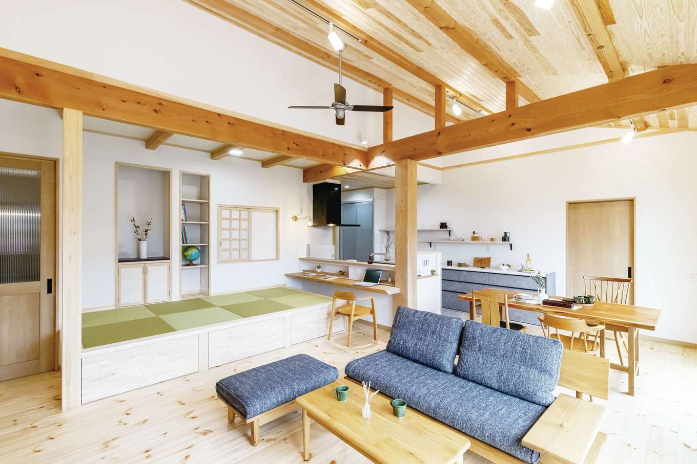 住まいるコーポレーション【自然素材、間取り、平屋】勾配天井が伸びやかなLDK。一つの空間にいながら、リビングやダイニング、畳スペースなど、それぞれの場所で違ったくつろぎ方ができる。小上がりに設けた障子戸を開けると洗面スペースにつながる