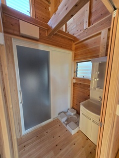 木の温もりを感じる脱衣スペース。明るい木目の壁と床が落ち着いた雰囲気を演出し、使いやすさにも配慮されたデザインである。