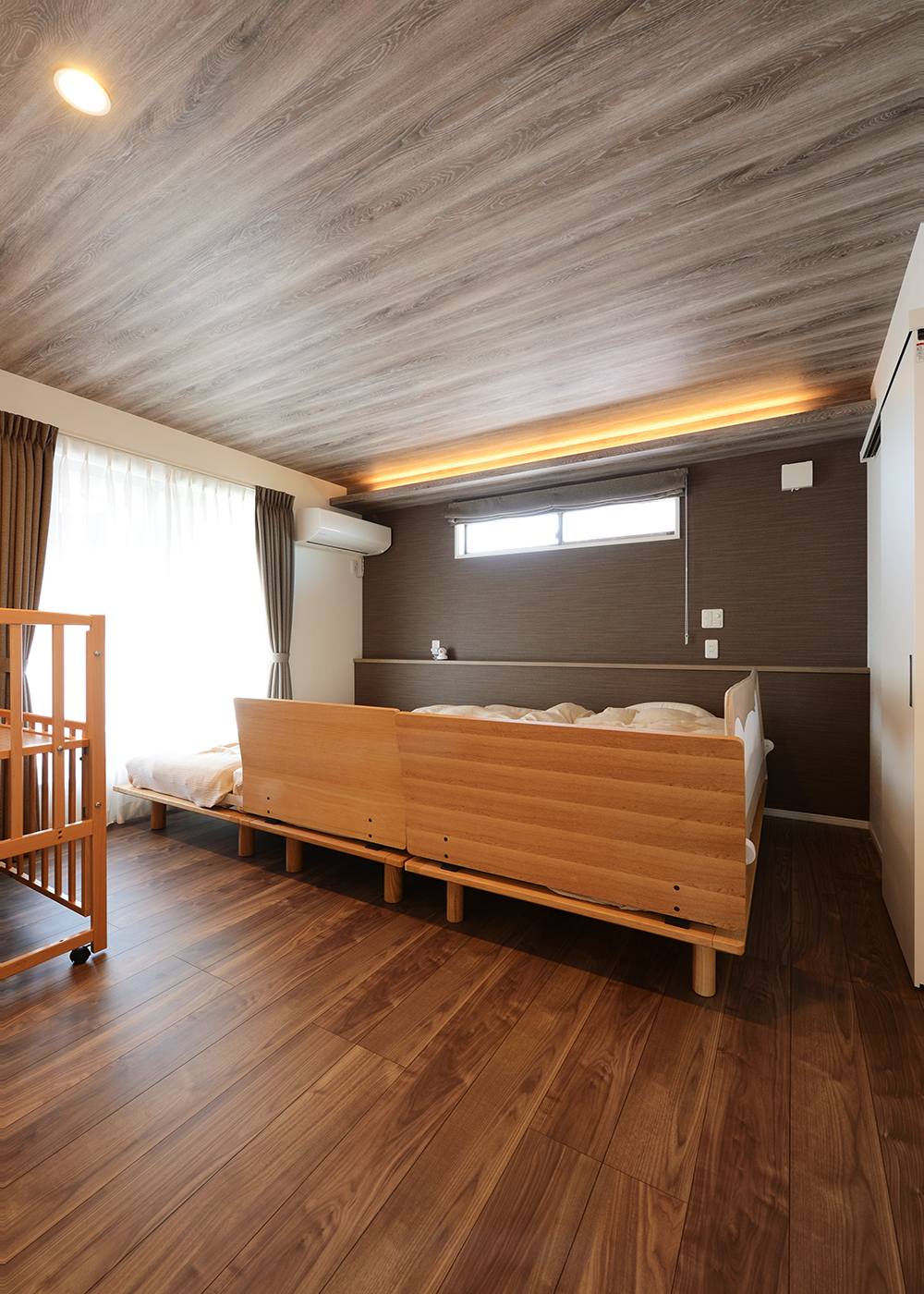 丸昇彦坂建設【デザイン住宅、子育て、間取り】ブラウンのクロス、木目、間接照明がシックで上品な印象を与える主寝室