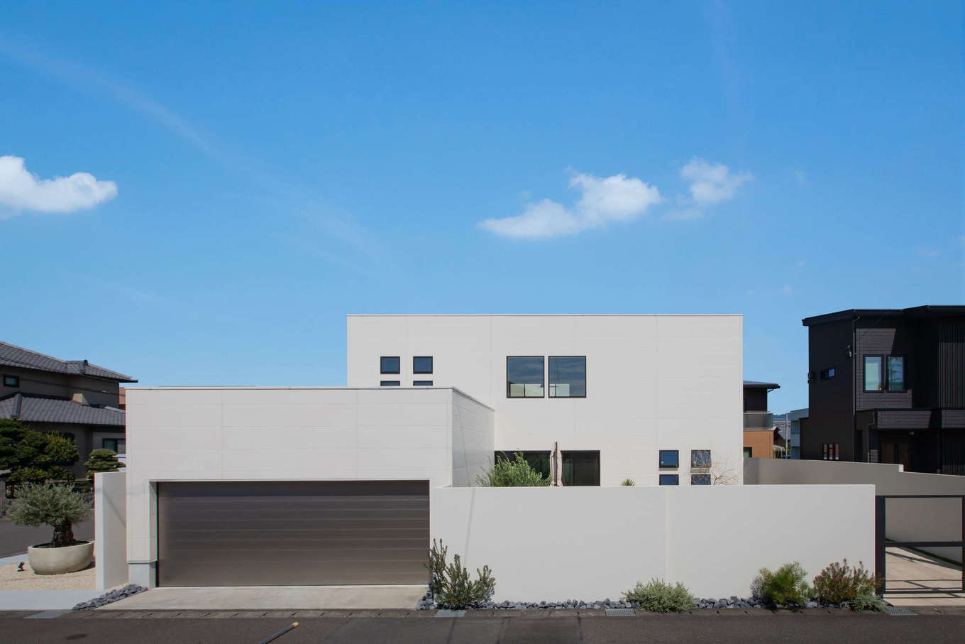 幸和ハウジング【デザイン住宅、夫婦で暮らす、ガレージ】シンプルな白い箱型の外観。ロックガーデンの植栽が外観を背景に美しく映える。夜は照明の灯りでリゾートホテルのように魅惑的な印象に！