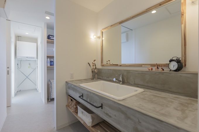 モルタル仕上げのオリジナル洗面台。鏡もカウンターもワイドサイズにして、朝の仕度が重なっても困らないようにした。奥さまもゆっくりとスキンケアやメイクを楽しめそう