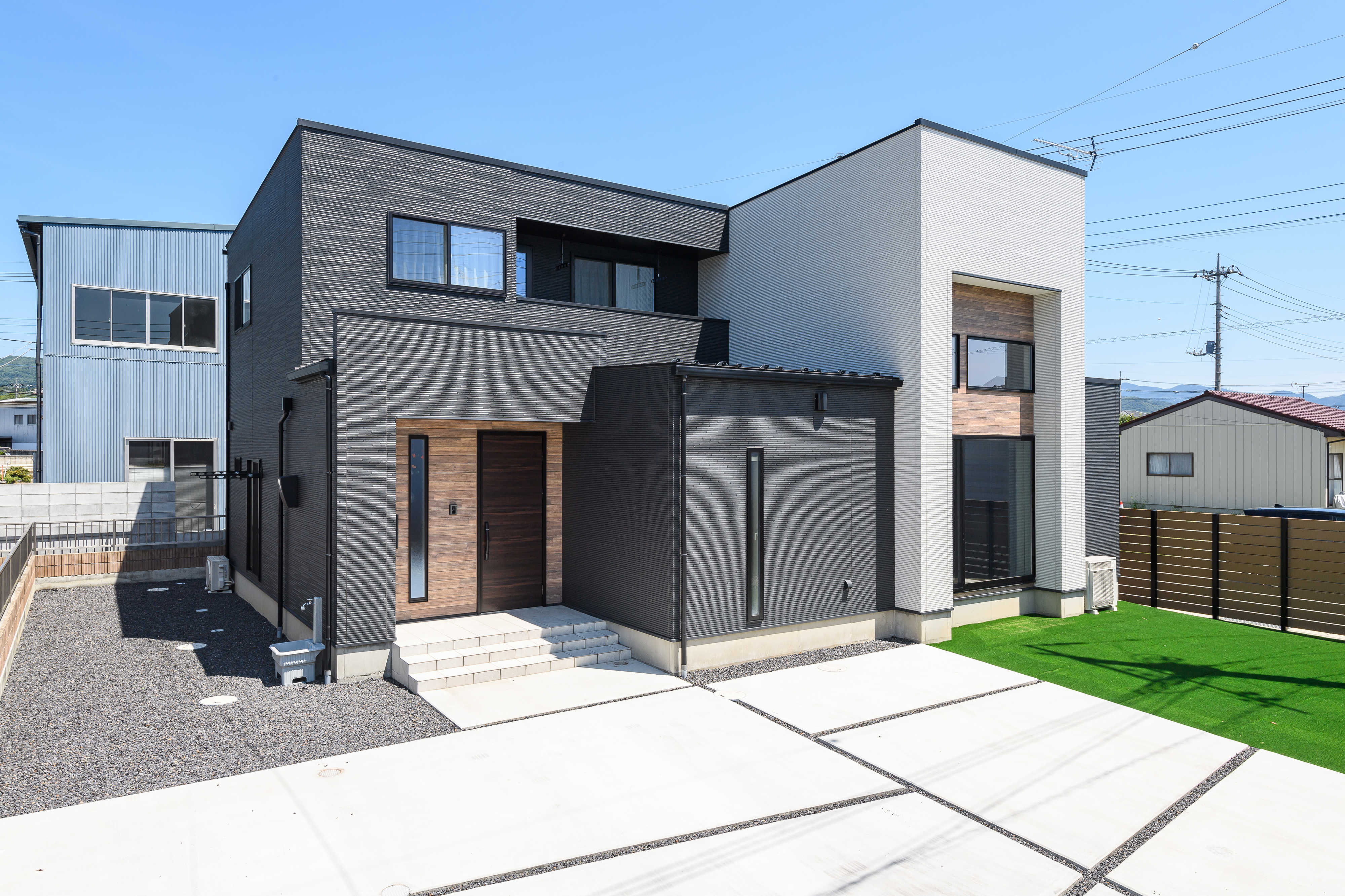 モデスト｜モダンなデザインの二階建て住宅。外壁にはシンプルな色調を用い、落ち着いた雰囲気を演出している。庭の緑が映える外観が目を引く。
