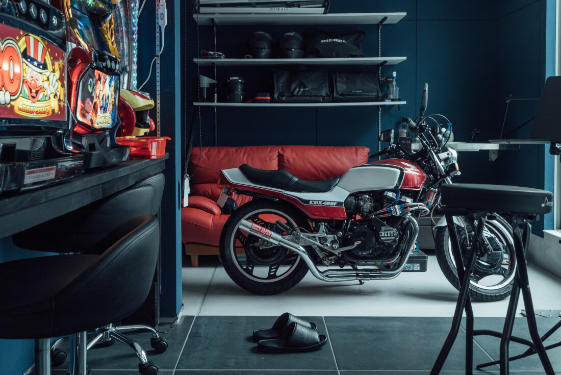 チェックハウス｜趣味のバイクが置かれたバイクガレージ。隣にはソファが配置され、リラックスしながら愛車を眺めるスペースが広がる
