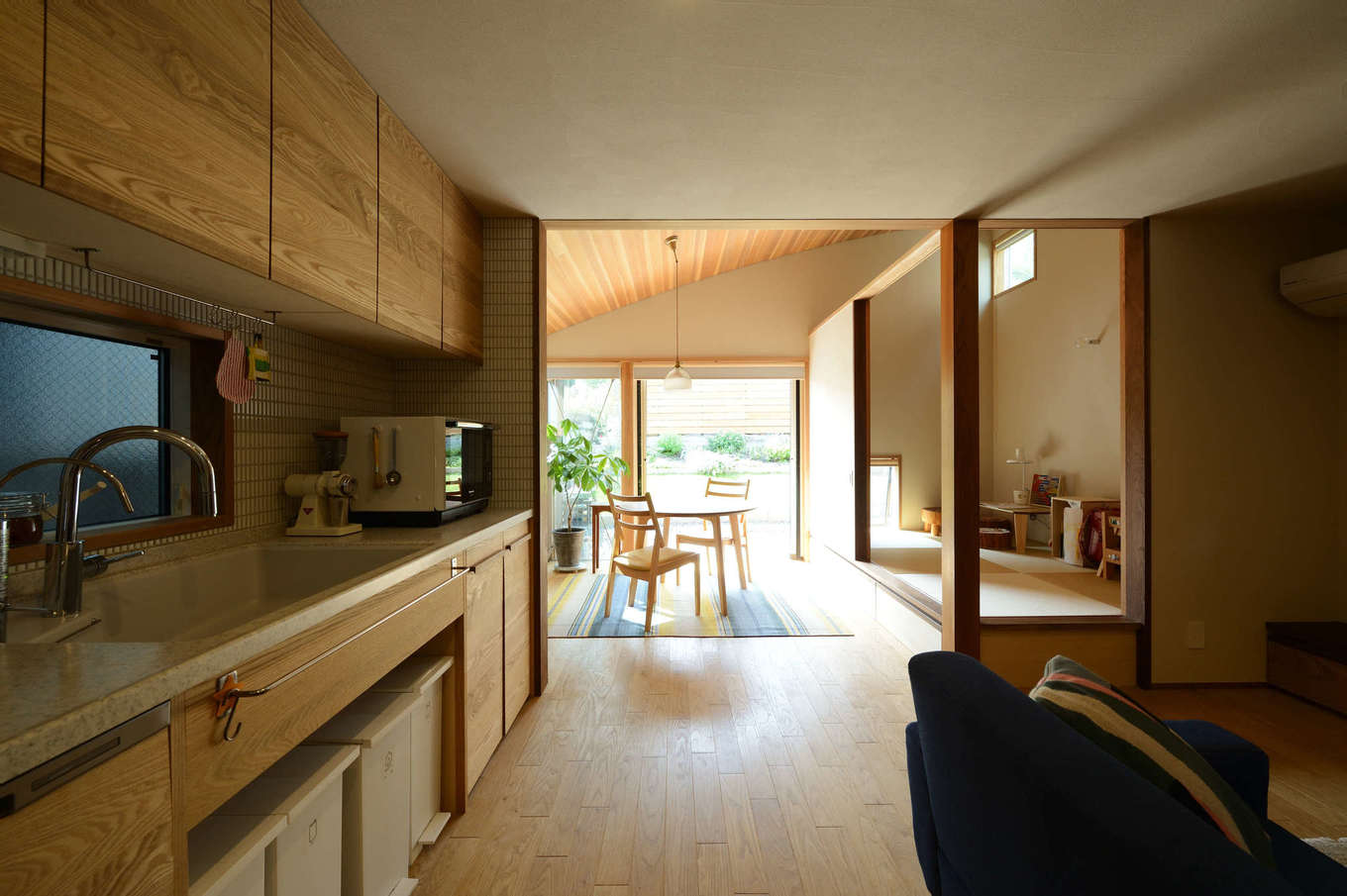 石牧建築【自然素材、狭小住宅、建築家】リビングの天井高を抑え、ダイニングを高い勾配天井にしたことで目線が遠くの庭へと抜け、実面積28坪以上に広く感じられる。キッチンは石牧社長のオリジナル造作で、システムキッチンよりもコストカットでき、使い勝手も抜群