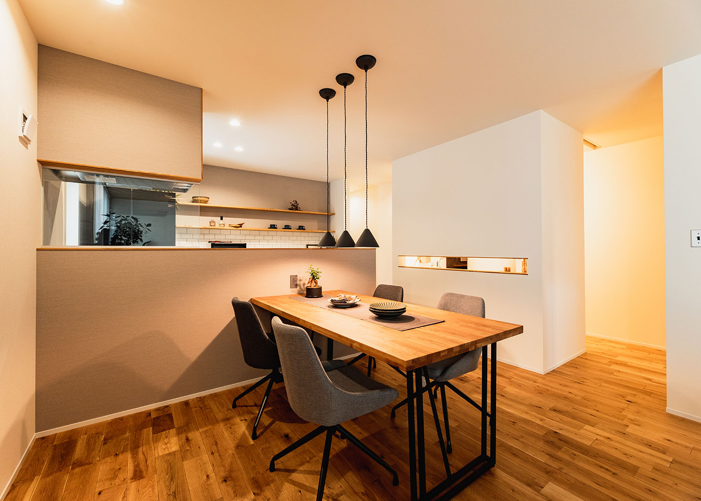 住家 JYUKA【デザイン住宅、間取り、平屋】グレーをベースに、白いタイルと造作棚でシンプルにまとめられたキッチン。水回りへの動線には周遊性をもたせ、家事効率をアップ。洗面台部分の壁を細長く開くことで、光と気配を行き来させている