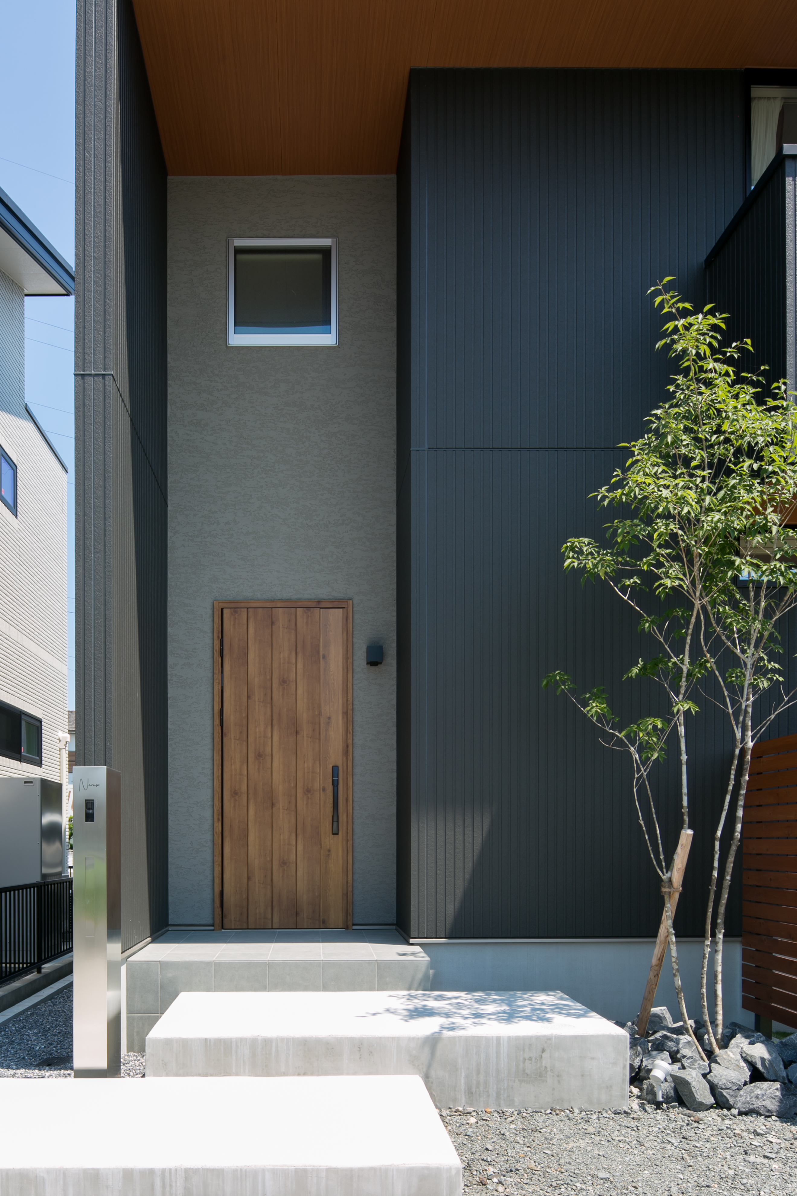 シンプル｜ドア背面は塗壁で仕上げシックな雰囲気に。
天井が高く開放感のある玄関となった。