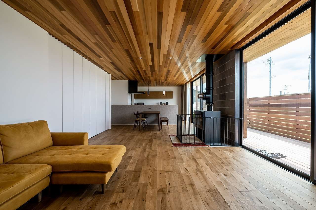 アーキテックス【デザイン住宅、省エネ、平屋】床の木目の向きに合わせて天井全面にレッドシダーを張った。これにより視線がずっと奥まで伸びていき、より開放的に感じられる。イエローのソファも木の空間にほどよく溶け込んでいる