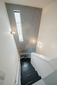 黒い踏板、壁一面に施したグレーのユーロスタッコ、漆喰の白がモダンな階段スペース