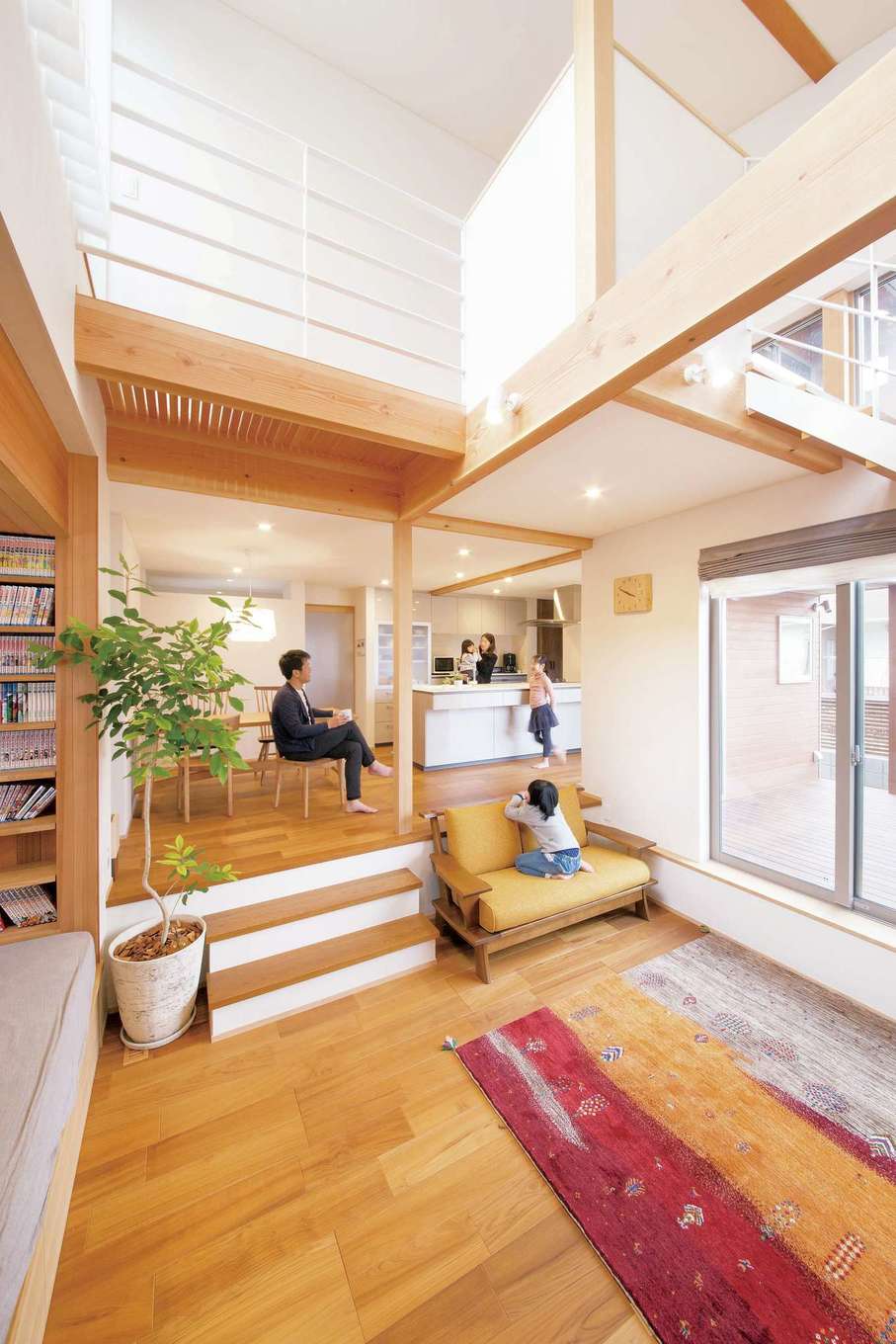 神谷綜合建設 カミヤの家【子育て、自然素材、スキップフロア】床暖房に対応した無垢のチーク材を使うことで、吹き抜けのある大空間の冷え問題も解決。一般的な家の床よりも低いので、ラグに座ると庭と空が視界いっぱいに広がる。