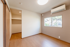 明るい自然光が差し込む寝室。床はナチュラルなウッド調で、部屋全体に温かみを感じる。奥には余裕のあるウォークインクローゼットも備わっている。