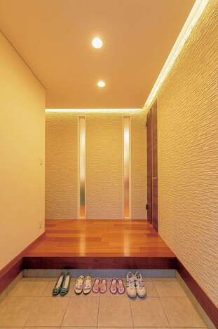 住宅工房 アリアンス｜塗り壁と間接照明の温かみに癒やされる玄関ホール。天井まで届くスリットの窓越しに家族の気配を感じるのがポイント