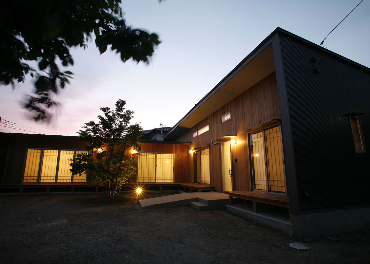タツホーム・竜建｜夕暮れ時に映えるモダンな平屋の外観。自然と調和したデザインで、植栽がアクセントとなり心地よい雰囲気を創り出している。