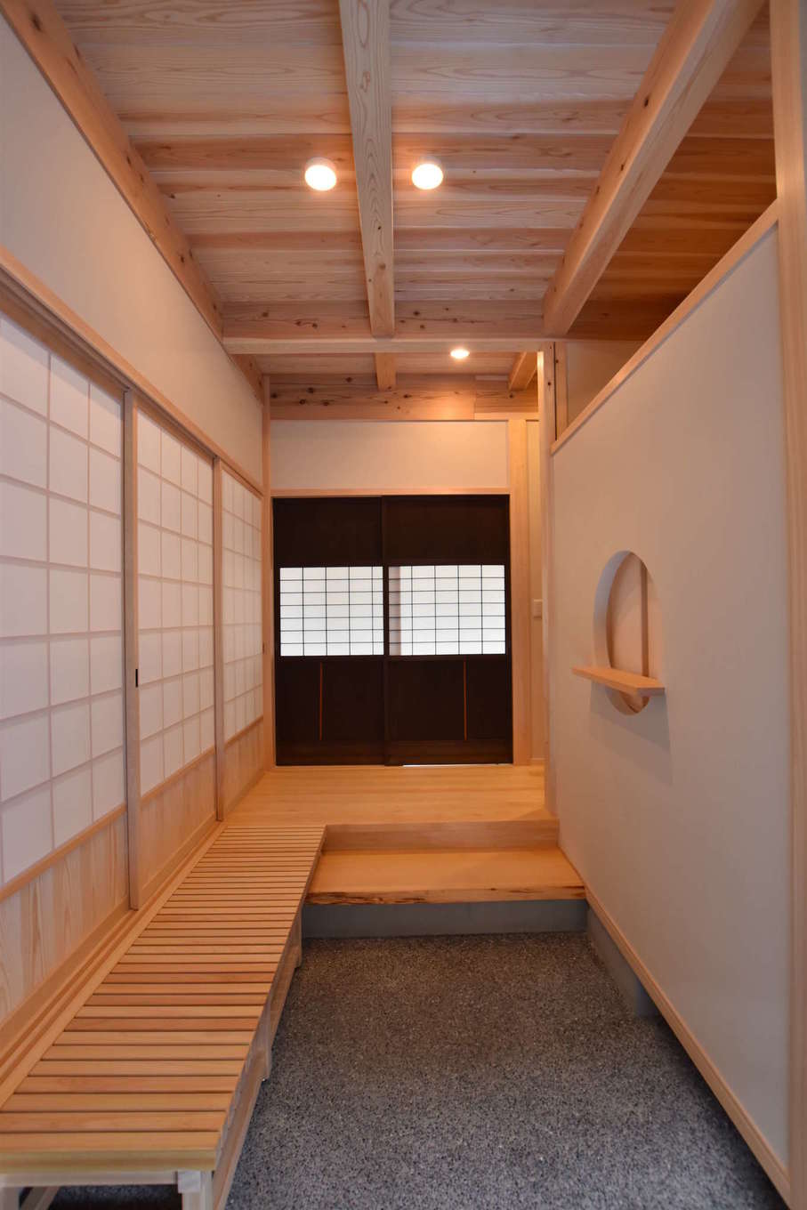 職人夢工房 TODA（戸田工務店）【和風、自然素材、間取り】洗い出しの土間と上質な無垢材、珪藻土で構成された玄関。正面の古建具は旧宅で使用されていたもの。三連の障子戸の先には、昔ながらの「田」の字型に和室が4室並んでいる。また、農作業の合間にも気軽に出入りできるように、玄関の隣に家族用の下足場とクロークが設けてある