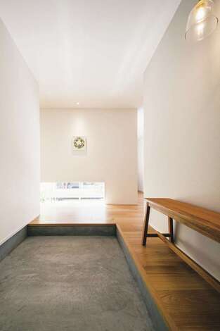 モルタルの玄関土間が白壁と調和した玄関。地窓から中庭の風景が垣間見え、視線が外へと抜ける。玄関ホールには木製のベンチを置くためのスペースも確保した