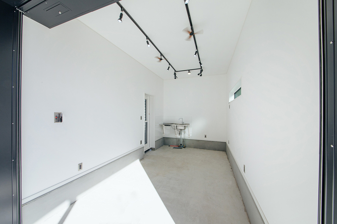 白い壁と天井で清潔感あるインナーガレージ。シンプルさが際立つデザインと便利な洗面台が設置されている