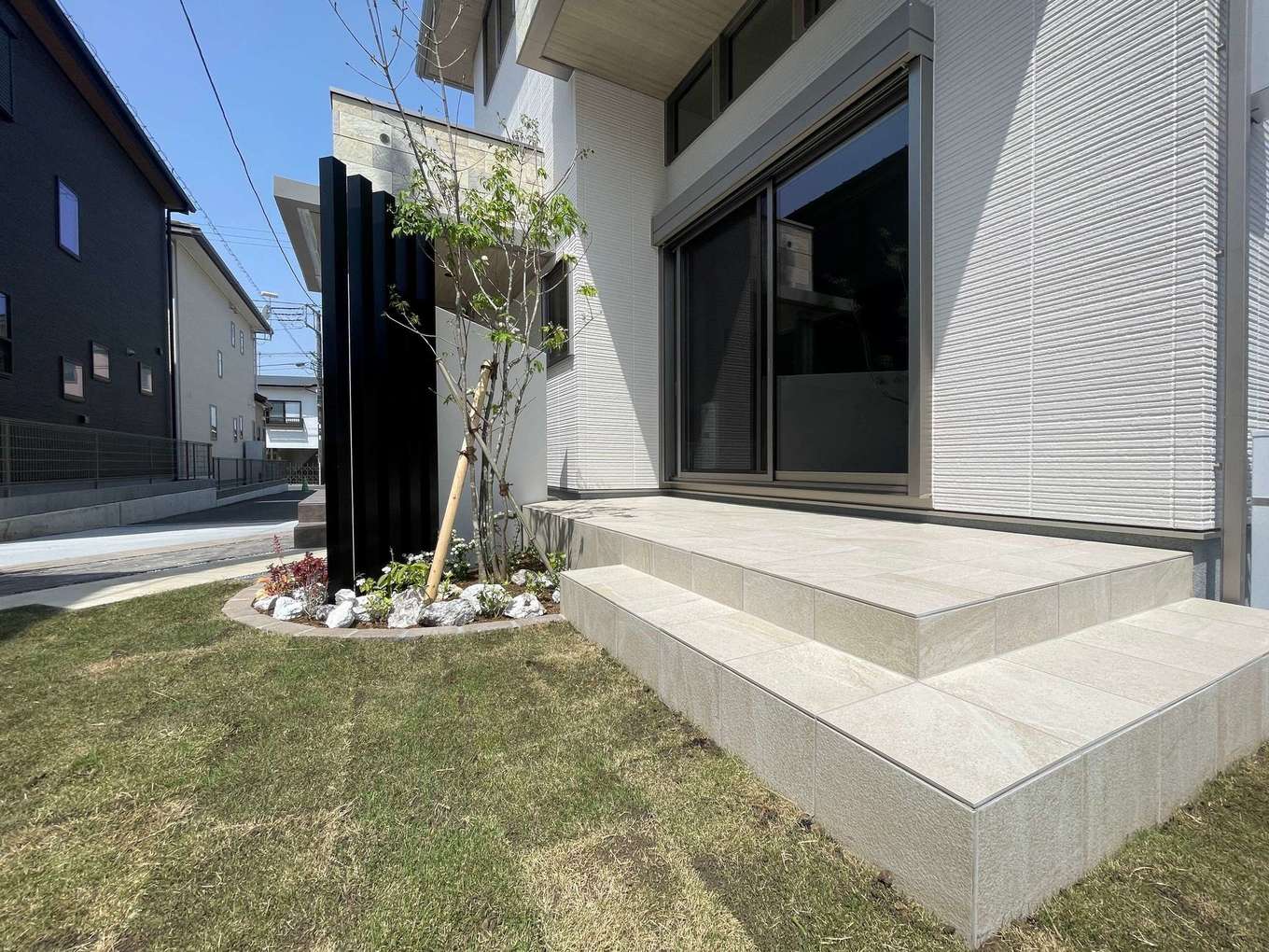 ミサワホーム静岡【デザイン住宅、間取り、建築家】重厚感を演出する大きなタイルデッキ。ブラックの枕木フェンスと緑の庭木が、外からの視線をさりげなくカットする。外構までトータルでコーディネートできる同社ならではの統一感ある仕上がりだ