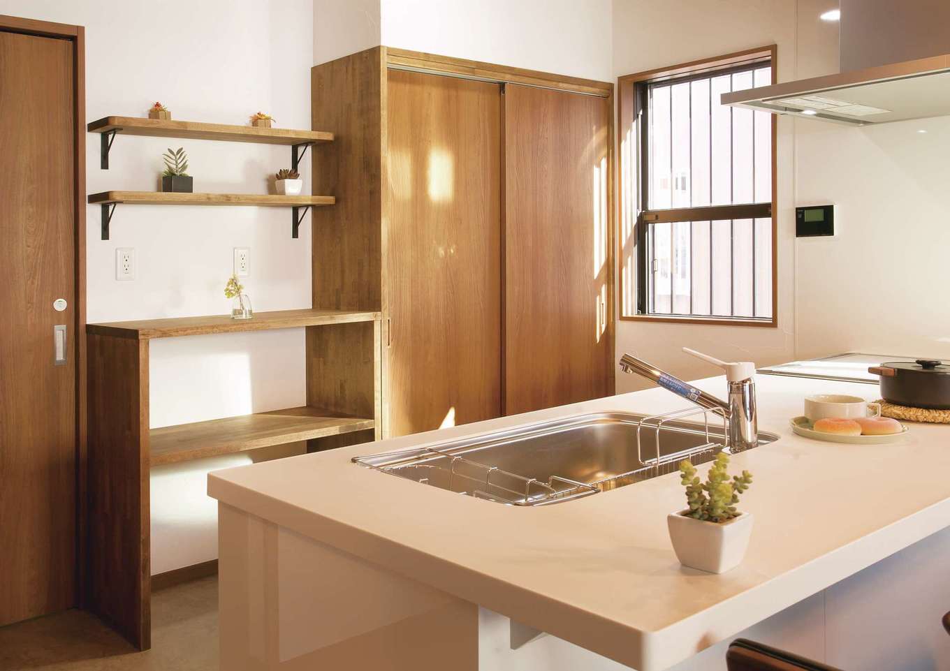 住まいるコーポレーション【デザイン住宅、自然素材、インテリア】ワイドなカウンタートップのオープンキッチン。背面の収納は床と同色で統一。生活感の出るものは大きな扉で「隠して収納」、オシャレな器類は棚に飾って「見せる収納」と、収納方法を上手に使い分けている