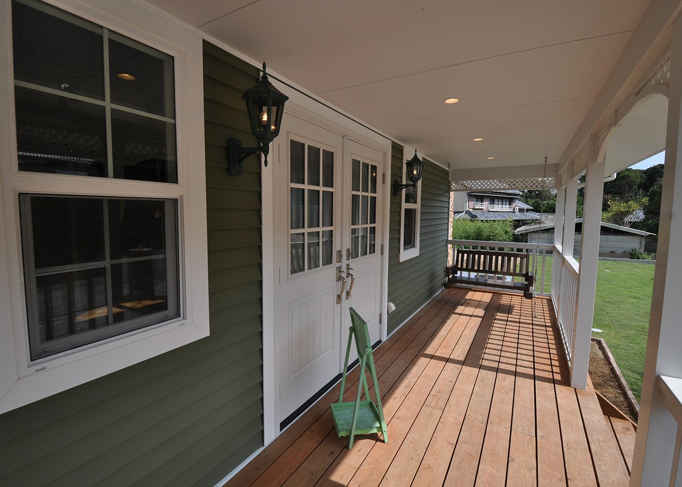 リンゾー【輸入住宅、ガレージ、デザイン住宅】長いカヴァードポーチはさまざまな過ごし方ができる。オリーブ色のラップサイディングと白い格子の入った窓のコントラストが美しい