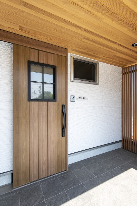 トキワハウス デザイン アンド ビルド（常盤工業）｜ナチュラルな雰囲気を持つ玄関。木製ドアと白い外壁が調和しており、温かみのあるエントランスを形成している