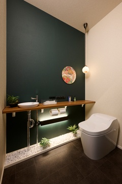 モダンなデザインのトイレ空間で、シックな壁紙とミニマルな照明が特徴的。植物が配され、落ち着いた雰囲気を演出している。