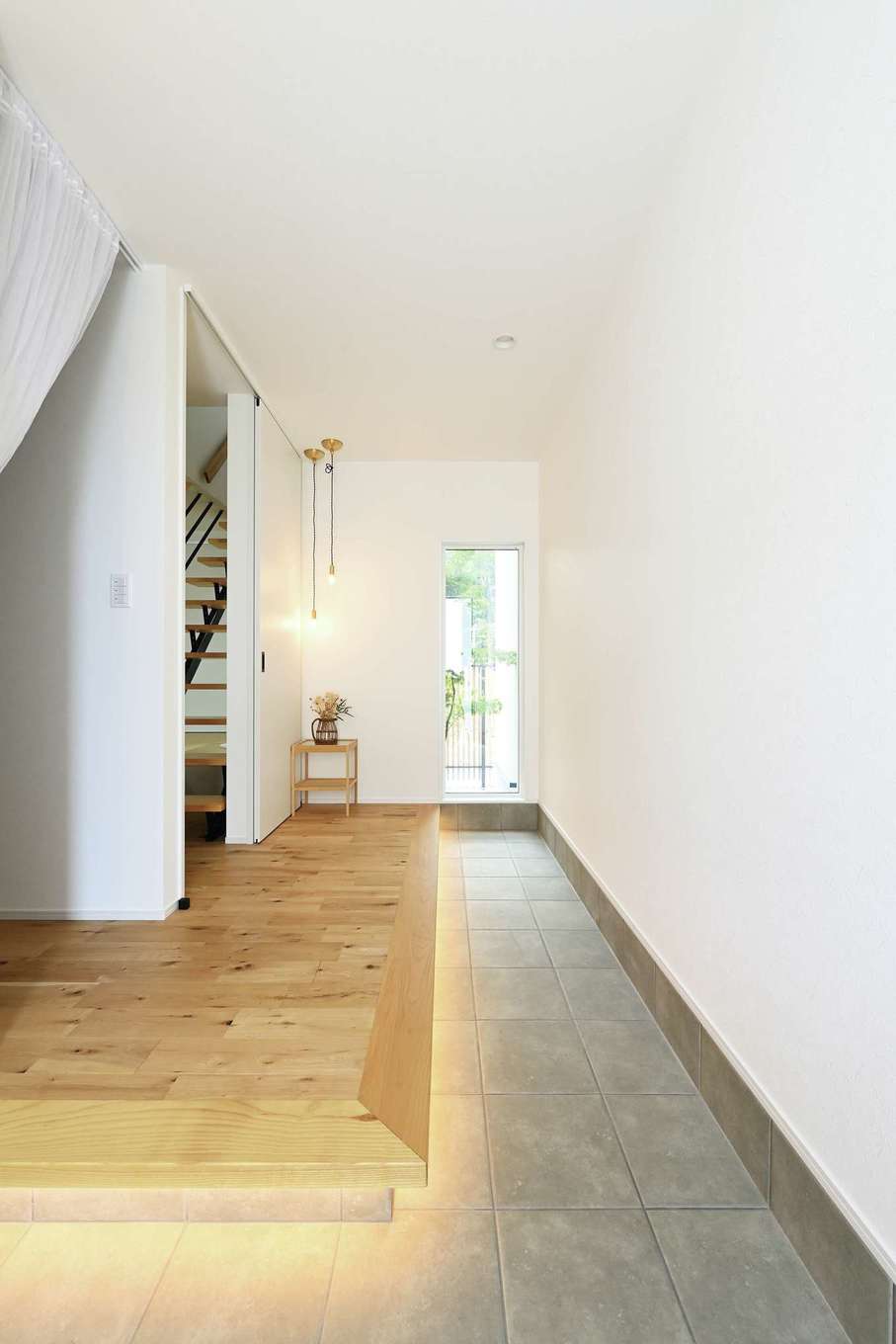 Yamaguchi Design 【デザイン住宅、省エネ、間取り】玄関に入ると土間が奥まで続き、窓の先には坪庭が見える。視線が外へ抜け、いっそう開放的に。間接照明やペンダント照明も効果的に活かされている