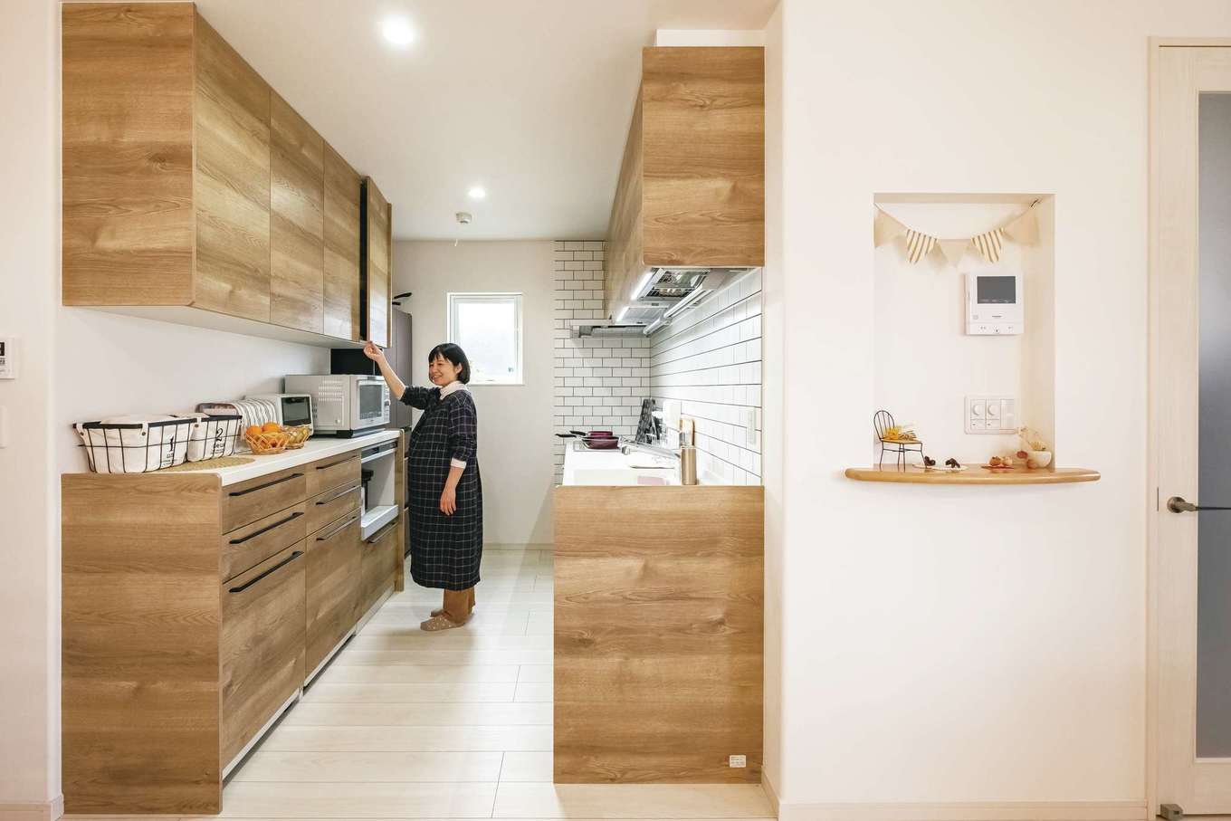 イデキョウホーム【デザイン住宅、省エネ、屋上バルコニー】リビングの見せ梁に合わせて選んだ木目調のキッチン。右側の壁は清潔感とデザイン性を兼ね備えた白タイルを張った
