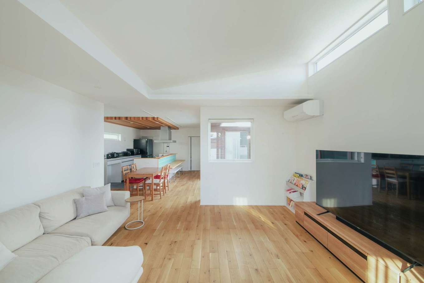 内田建設【デザイン住宅、建築家、平屋】ワンフロアでつながりを持たせながら、緩やかにゾーニングされたLDK。リビングを勾配天井にしたことでダイニングと目の高さが変わり、より広く感じられる。建物をコの字型に配置して、中庭から十分な光と風を取り込む。照明をあえてダウンライトだけに限定し、シンプルで美しい空間演出を楽しめるようにした