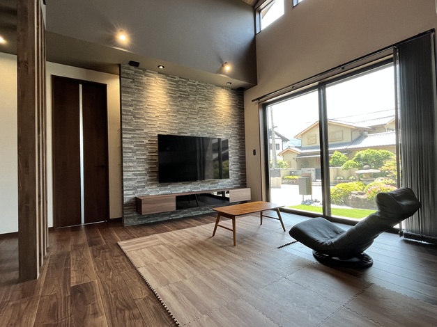 広々としたリビングは、落ち着いた色調の内装と大きな窓からの光が開放感を演出している。壁掛けテレビが視覚的なアクセントになっている。
