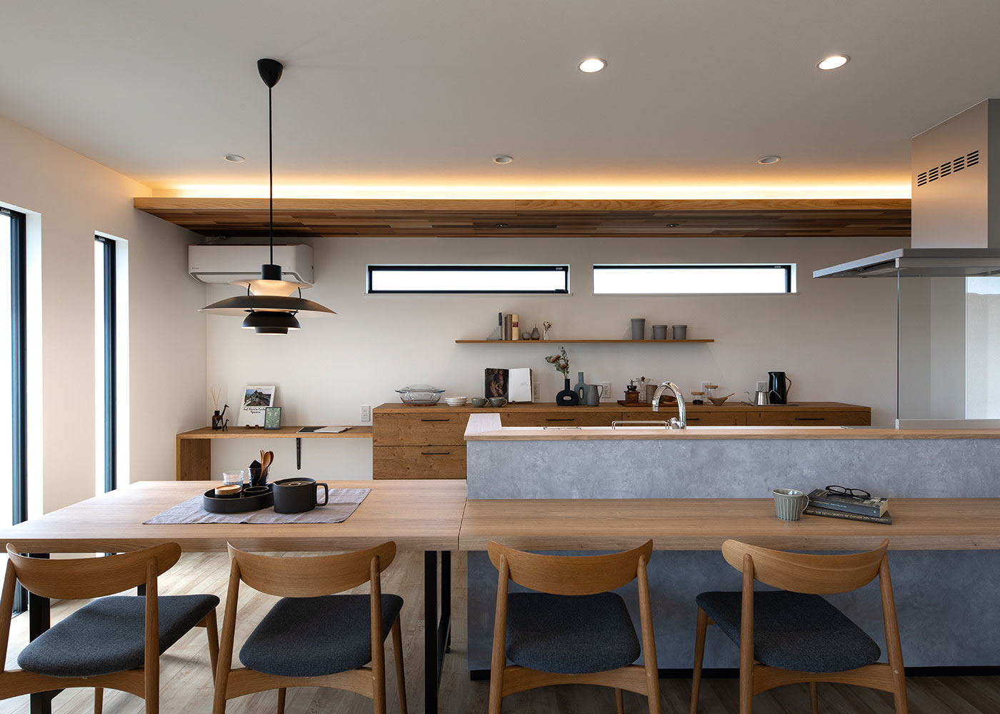 KUREKEN HAUS（榑林建設）【デザイン住宅、収納力、ペット】ダイニングキッチンは、木調の下がり天井と間接照明が、カフェのような空間。一目惚れして購入した「ルイスポールセン」のペンダントライトも雰囲気たっぷりだ。キッチンを囲むように配置したダイニングテーブルも使いやすい。左手奥には、ちょっとした事務作業に、子どものスタディスペースにと多用途に活躍するカウンターを用意