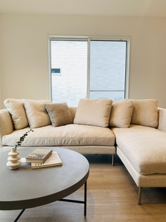 シンプルでモダンなリビングスペース。大きなL字型ソファが部屋の中心に配置され、リラックスした雰囲気を演出している。