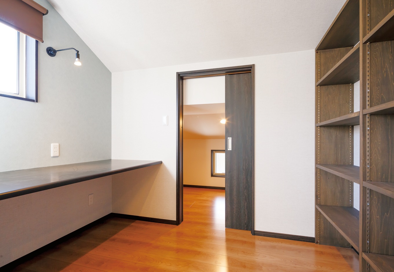 エコハウジング【収納力、自然素材、間取り】主寝室の一角に設けた書斎コーナー。カウンターと本棚は造作。引戸を開けると、大容量の小屋裏収納