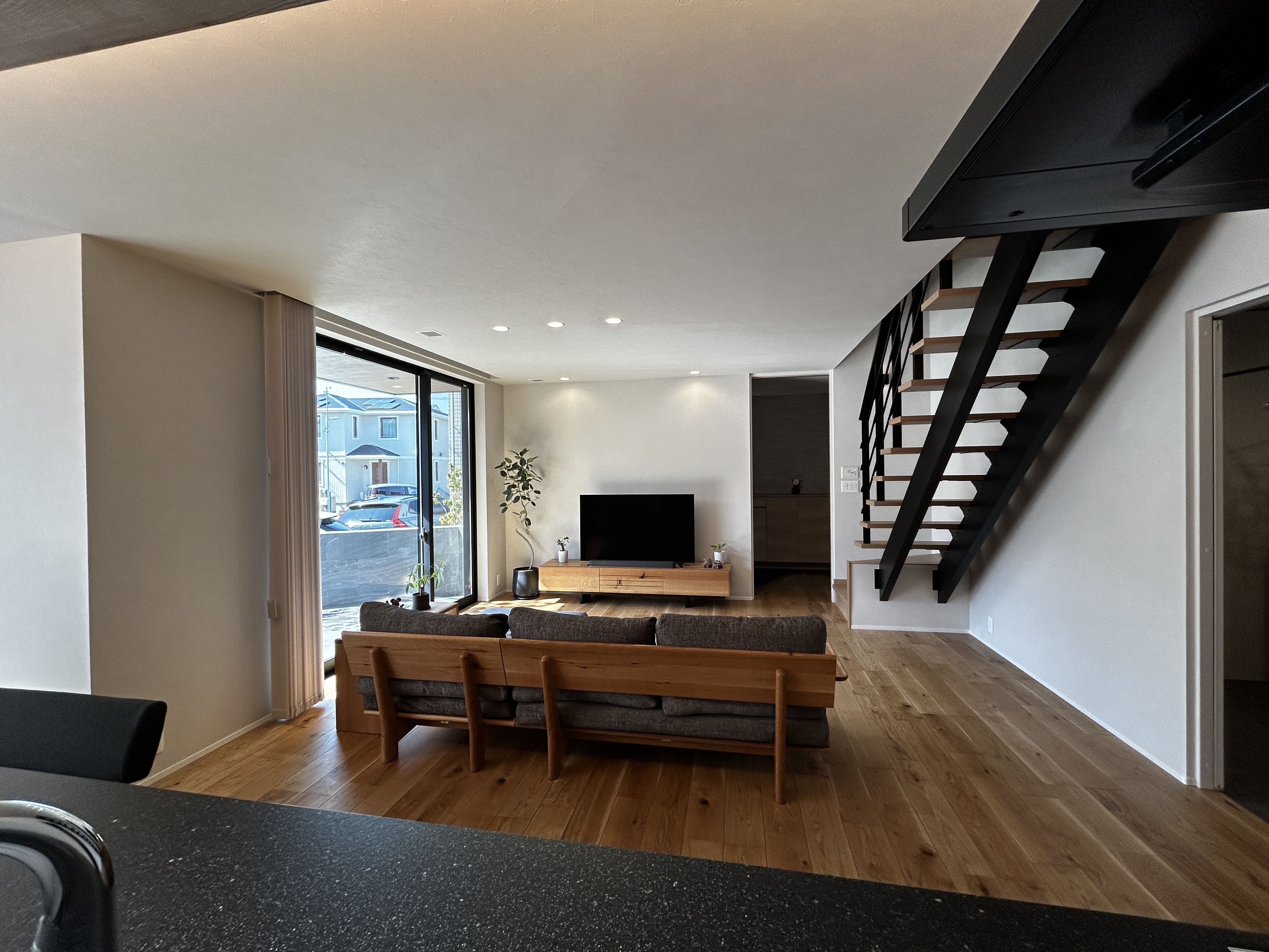 パナソニックホームズ中部第一支社 愛知第一支店・愛知第二支店｜オープンなリビングダイニングは木製のフローリングとシックな家具でまとめられ、階段のデザインが印象的である。大きな窓からは自然光が入り、開放感が溢れている。  