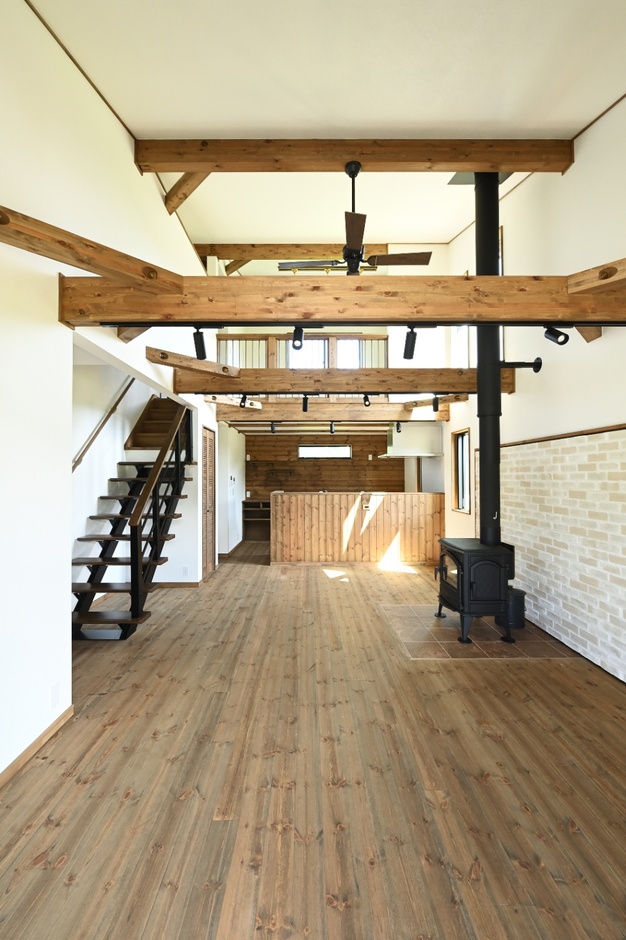 開放感あふれるリビングダイニング。木の梁と薪ストーブが配置された、くつろぎのスペース。